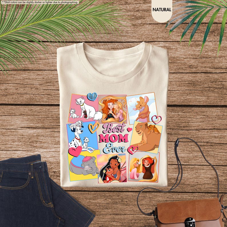 Pode incluir: Uma camiseta bege com uma colagem de personagens de desenhos animados e o texto "Best Mom Ever". Os personagens incluem um d&aacute;lmata, um le&atilde;o, um gato e uma princesa.