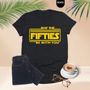 May include: Black t-shirt with a yellow graphic that says "May the Fifties Be With You".