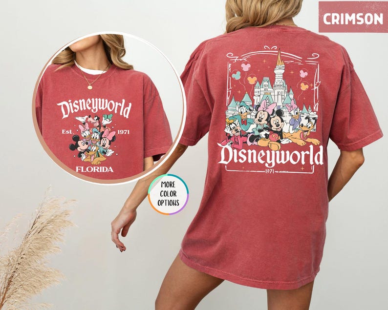 Puede incluir: Camiseta de color carmes&iacute; con un dise&ntilde;o de Disneyworld. La parte delantera presenta a Mickey, Minnie, Donald y otros personajes con el texto "Disneyworld Florida Est. 1971." La parte trasera muestra un castillo y personajes con "Disneyworld 1971."