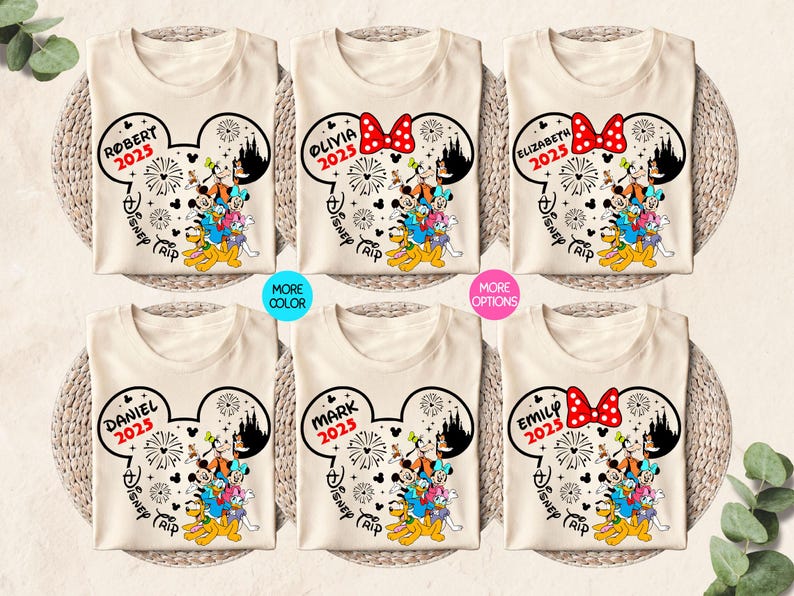 May include: Six beige t-shirts with a Mickey Mouse head design. Each shirt has a different name and the year 2025 printed on it. The shirts say "Robert", "Olivia", "Elizabeth", "Daniel", "Mark", and "Emily". Each shirt also says "Disney Trip" underneath the name.