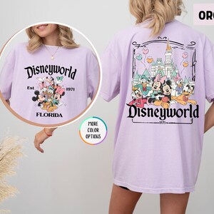 Puede incluir: Camiseta color orqu&iacute;dea con un gr&aacute;fico de Disneyworld en la parte delantera y trasera. El gr&aacute;fico frontal presenta personajes de Disney y el texto "Disneyworld Est. 1971 Florida". El gr&aacute;fico trasero muestra el castillo de Disney y personajes.