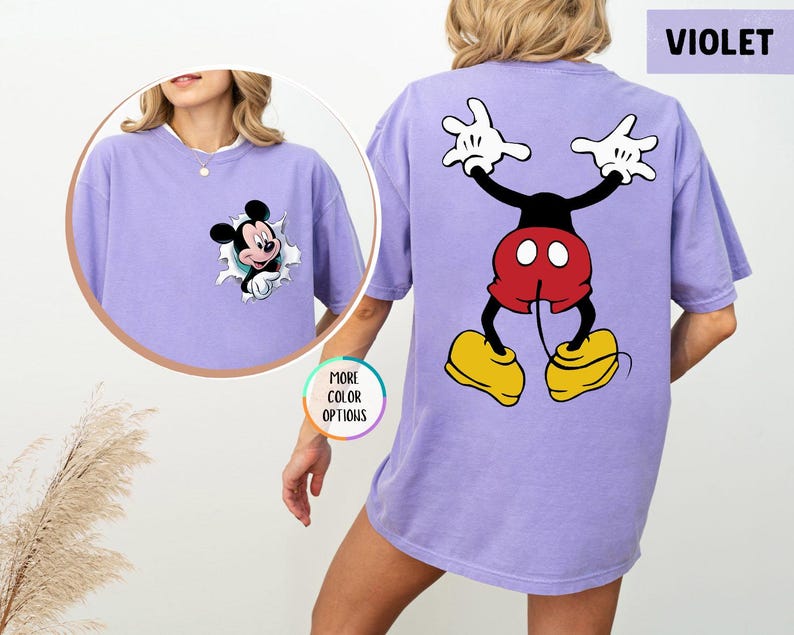 May include: A violet-coloured t-shirt with Mickey Mouse graphics. The front features Mickey breaking through a hole, and the back shows Mickey in a playful pose. The shirt has a comfortable, oversized fit.