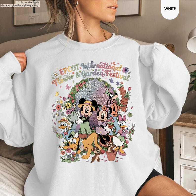 May include: White sweatshirt featuring a colorful graphic of Disney characters, including Mickey and Minnie Mouse, Goofy, and Donald Duck, surrounded by flowers and the text "EPCOT International Flower & Garden Festival."