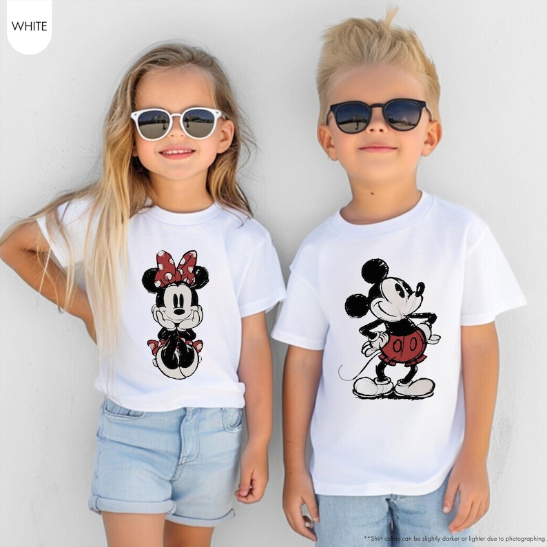 May include: Two children wearing white t-shirts with Disney character graphics. One shirt features Minnie Mouse with a red polka dot bow, and the other features Mickey Mouse in a red outfit. Both are wearing sunglasses.