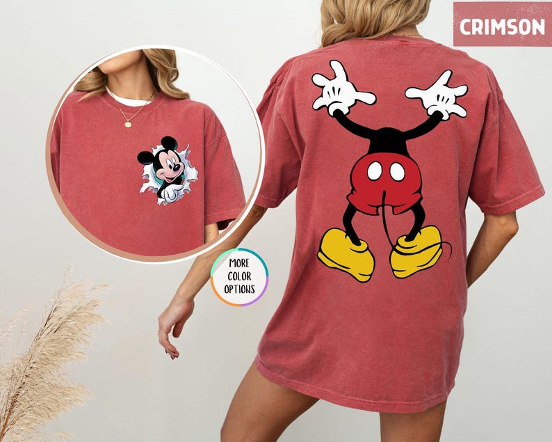 May include: Crimson-coloured t-shirt with a Mickey Mouse graphic. The front shows Mickey emerging from a torn hole, and the back displays a full-body cartoon image of Mickey Mouse. The shirt has short sleeves and a relaxed fit. The word 'CRIMSON' is in the top right corner.