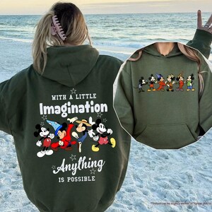 Puede incluir: Una sudadera con capucha verde oliva con un gr&aacute;fico de Mickey Mouse y sus amigos. La parte posterior de la sudadera con capucha tiene el texto "WITH A LITTLE Imagination Anything IS POSSIBLE". La parte delantera de la sudadera con capucha tiene un gr&aacute;fico m&aacute;s peque&ntilde;o de los personajes.