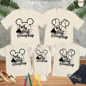Pode incluir: Conjunto de quatro t-shirts bege com orelhas de Mickey Mouse pretas e o texto "My first DISNEptrip" e uma silhueta preta do castelo da Cinderela. As t-shirts s&atilde;o de tamanhos diferentes para adultos e crian&ccedil;as.