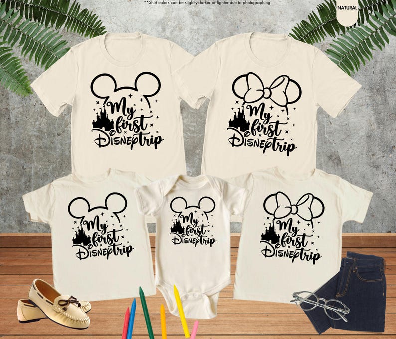 Pode incluir: Conjunto de quatro t-shirts bege com orelhas de Mickey Mouse pretas e o texto "My first DISNEptrip" e uma silhueta preta do castelo da Cinderela. As t-shirts s&atilde;o de tamanhos diferentes para adultos e crian&ccedil;as.