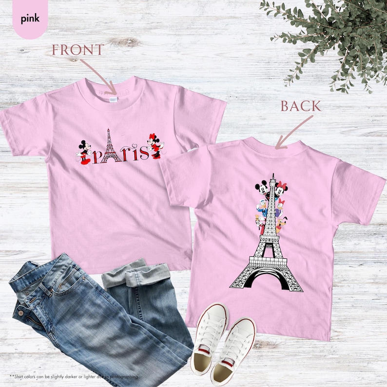 Pu&ograve; includere: T-shirt rosa chiaro con la Torre Eiffel e la scritta "Paris" con personaggi dei cartoni animati. Il retro della maglietta mostra la Torre Eiffel con personaggi dei cartoni animati. La maglietta &egrave; abbinata a jeans blu e scarpe da ginnastica bianche.