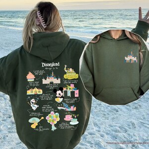 a woman wearing a green disneyland hoodie on the beach