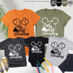Pode incluir: Conjunto de cinco t-shirts com uma silhueta preta de orelhas do Mickey Mouse com o texto "My first Disneytrip" em preto e branco. As t-shirts s&atilde;o de v&aacute;rias cores, incluindo laranja, cinza, preto e verde.