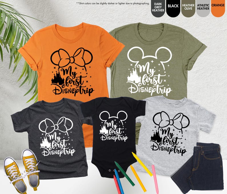 Pode incluir: Conjunto de cinco t-shirts com uma silhueta preta de orelhas do Mickey Mouse com o texto "My first Disneytrip" em preto e branco. As t-shirts s&atilde;o de v&aacute;rias cores, incluindo laranja, cinza, preto e verde.