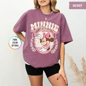 May include: A mauve t-shirt with a vintage-style graphic of Minnie Mouse holding a teacup. The graphic features the text "Minnie Mouse" in a pink and white floral design.