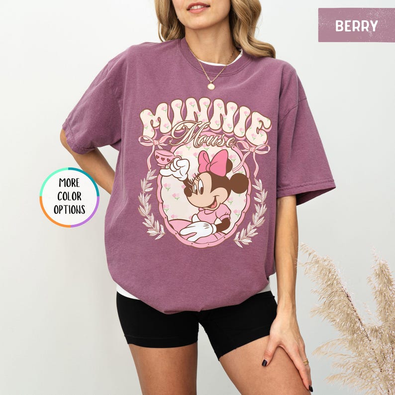 May include: A mauve t-shirt with a vintage-style graphic of Minnie Mouse holding a teacup. The graphic features the text "Minnie Mouse" in a pink and white floral design.