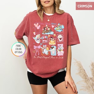 May include: Crimson-colored t-shirt featuring a colorful graphic of Disney characters and icons. The design includes Mickey and Minnie Mouse, Dumbo, and other elements. The text "Walt Disney World" and "The Most Magical Place on Earth" are also visible.