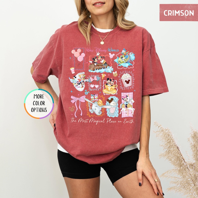 May include: Crimson-colored t-shirt featuring a colorful graphic of Disney characters and icons. The design includes Mickey and Minnie Mouse, Dumbo, and other elements. The text "Walt Disney World" and "The Most Magical Place on Earth" are also visible.