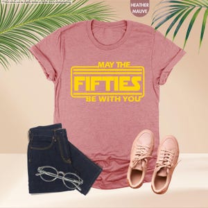 May include: A heather mauve t-shirt with a yellow graphic that says "May the Fifties Be With You".