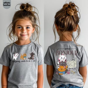 May include: Athletic heather gray t-shirt featuring a cartoon design of three cats with the text "everybody wants to be a cat". The back of the shirt has a design with the text "Bonjour" and the Eiffel Tower. The shirt is worn by a young girl.