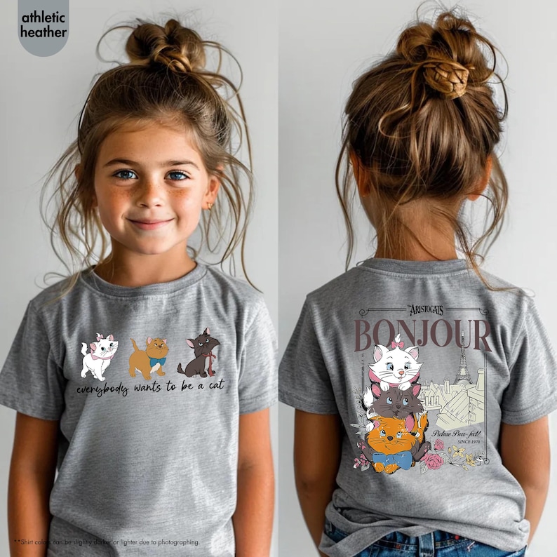 May include: Athletic heather gray t-shirt featuring a cartoon design of three cats with the text "everybody wants to be a cat". The back of the shirt has a design with the text "Bonjour" and the Eiffel Tower. The shirt is worn by a young girl.