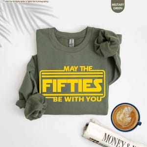 May include: A green sweatshirt with the text "May the Fifties Be With You" in a yellow Star Wars-inspired font.