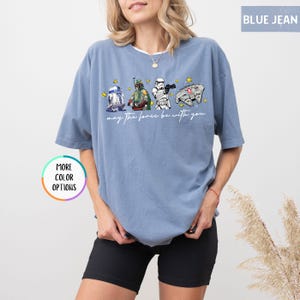 Puede incluir: Camiseta azul vaquero con un gr&aacute;fico de Star Wars con R2-D2, Boba Fett, un Stormtrooper y el Halc&oacute;n Milenario. El texto "may the force be with you" est&aacute; impreso debajo. La camiseta tiene mangas cortas.