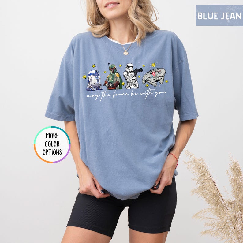 Puede incluir: Camiseta azul vaquero con un gr&aacute;fico de Star Wars con R2-D2, Boba Fett, un Stormtrooper y el Halc&oacute;n Milenario. El texto "may the force be with you" est&aacute; impreso debajo. La camiseta tiene mangas cortas.