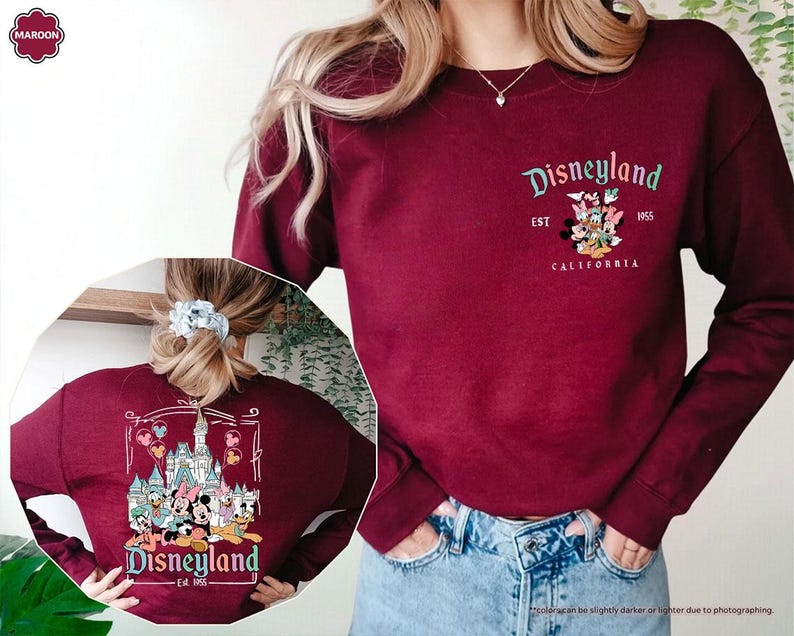 May include: Maroon sweatshirt with a Disneyland graphic featuring Mickey Mouse and friends. The text on the sweatshirt reads "Disneyland Est. 1955 California". The back of the sweatshirt features a cartoon image of Disneyland with Mickey Mouse and friends.