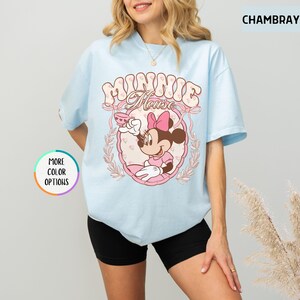 May include: A light blue t-shirt with a pink and white graphic of Minnie Mouse holding a teacup. The graphic includes the text "Minnie Mouse" in a retro font.