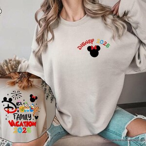 K&ouml;nnte beinhalten: Ein sandfarbener Pullover mit dem Text "Disney 2025" und einer Mickey-Maus-Silhouette auf der Vorderseite. Die R&uuml;ckseite des Pullovers zeigt eine bunte Grafik mit dem Text "Disney Family Vacation 2025".