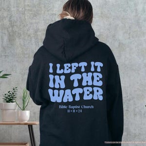 May include: Black hoodie with the text "I LEFT IT IN THE WATER" in light blue, with "Bible Baptist Church" and the date "11-11-24" below. The hoodie is displayed on a person's back.