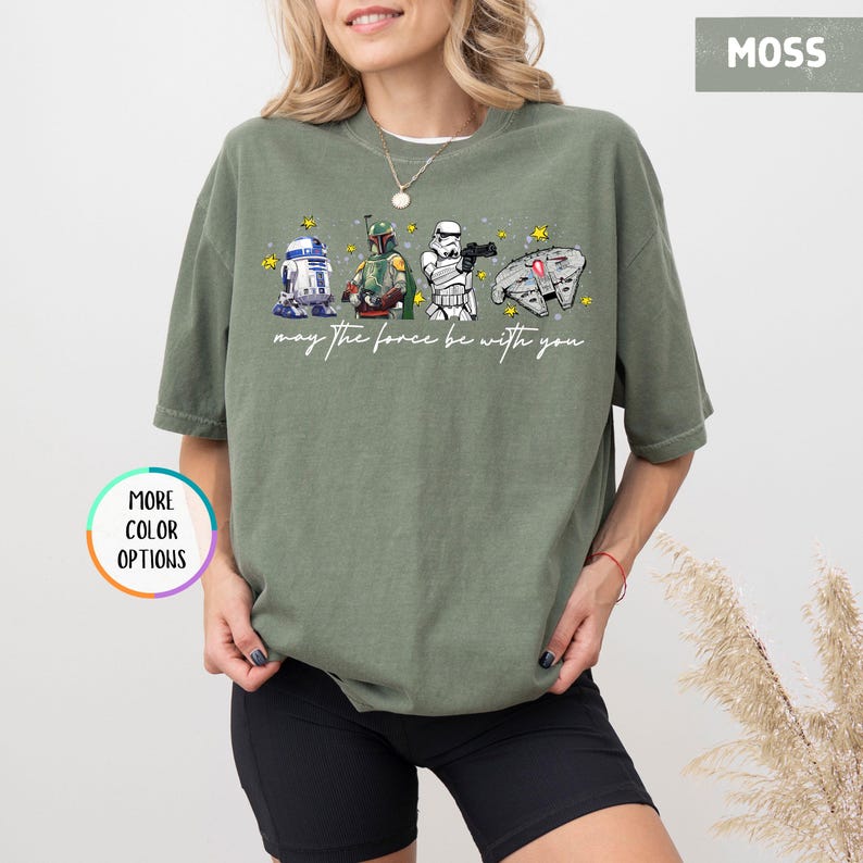 Puede incluir: Camiseta verde musgo con personajes de Star Wars: R2-D2, Boba Fett, un Stormtrooper y el Halc&oacute;n Milenario. La frase "may the force be with you" est&aacute; escrita en cursiva. Estrellas amarillas dispersas alrededor de los personajes.