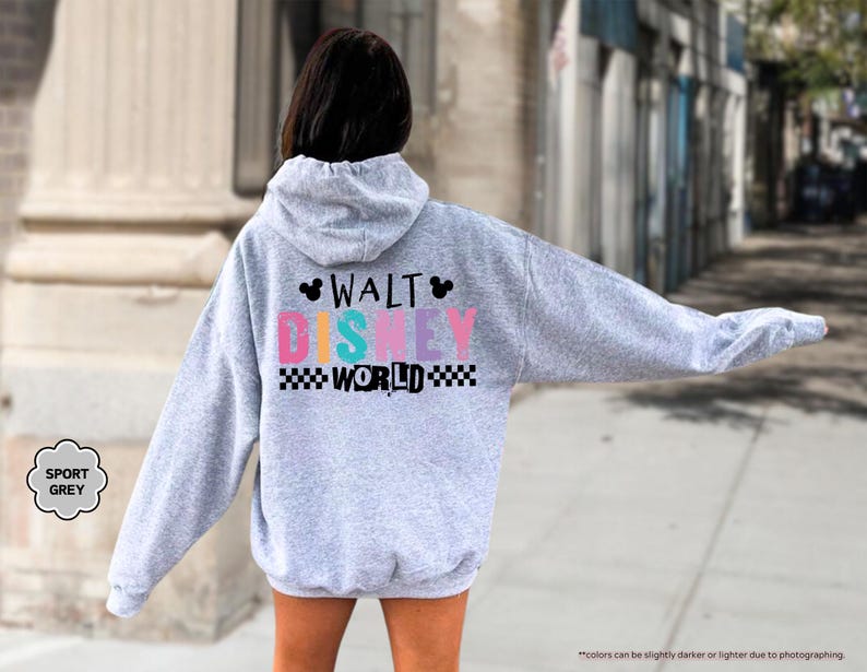 Puede incluir: Una sudadera con capucha gris claro con el texto "WALT DISNEY WORLD" en letras coloridas y un patr&oacute;n de cuadros blanco y negro. La sudadera con capucha tiene una capucha y mangas largas. Las palabras "SPORT GREY" est&aacute;n en un c&iacute;rculo gris.