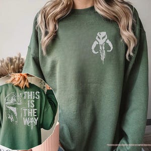 May include: A green sweatshirt with a white Mandalorian symbol on the front and the text "This is the way" on the back.