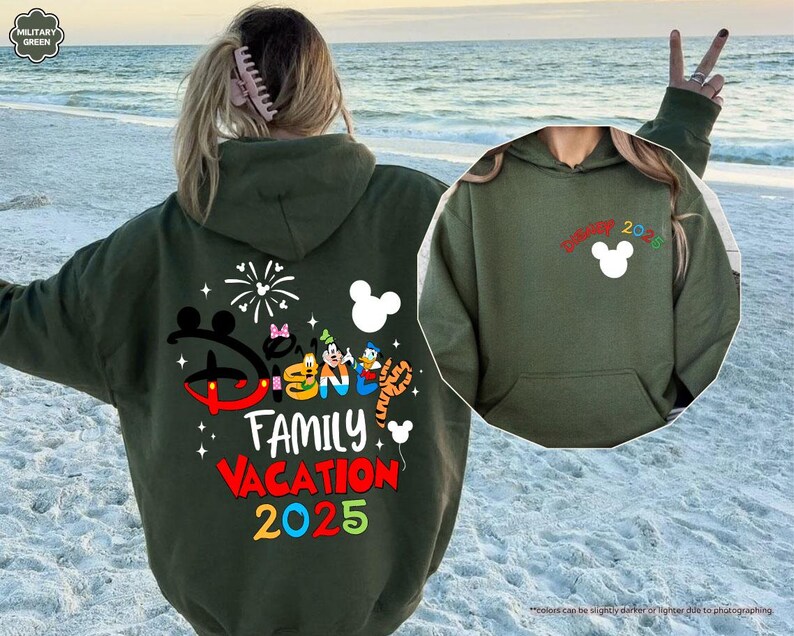 K&ouml;nnte beinhalten: Gr&uuml;ner Kapuzenpullover mit einem Disney Family Vacation 2025-Motiv auf der R&uuml;ckseite und einem Mickey Mouse-Motiv auf der Vorderseite. Der Pullover hat eine Kapuze mit Kordelzug und eine K&auml;ngurutasche.