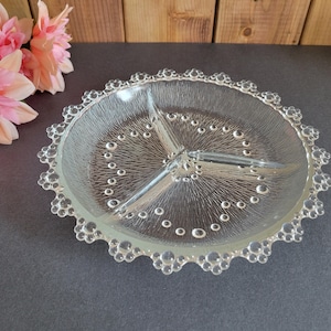 May include: A clear, divided glass serving dish with a textured interior and a scalloped edge. The dish is divided into three sections and features a bubble-like design around the rim. The dish is approximately 23 cm in diameter.