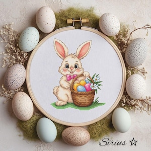 May include: A white bunny rabbit holding a basket of colorful Easter eggs. The bunny is wearing a pink bow tie and is standing on a green patch of grass. The basket is brown and has a white handle. The eggs are red, yellow, blue, green, and purple.