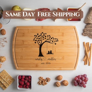 May include: A personalized bamboo cutting board with a laser engraved design of a tree with hearts and two cats on a swing. The text "emily ♥ miller est. 2019" is engraved below the design.