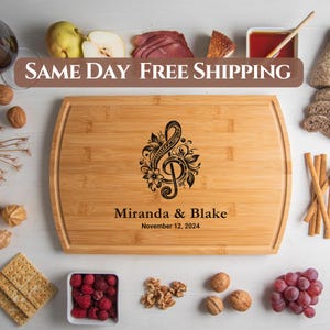 May include: Personalized bamboo cutting board with a black engraved treble clef design and floral accents. The board is engraved with the names "Miranda & Blake" and the date "November 12, 2024".