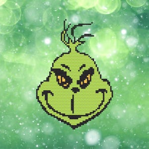 Puede incluir: Un diseño verde de punto de cruz de una cara con una sonrisa traviesa y ojos amarillos. El diseño está delineado en negro y se establece sobre un fondo verde borroso con motas blancas, creando un tema festivo de vacaciones.