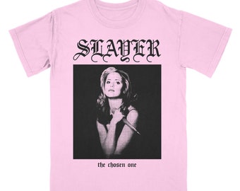 Può includere: T-shirt rosa chiaro con la scritta "SLAYER" in carattere gotico sopra un'immagine in bianco e nero di una donna che tiene un coltello. Sotto l'immagine c'è la scritta "the chosen one".