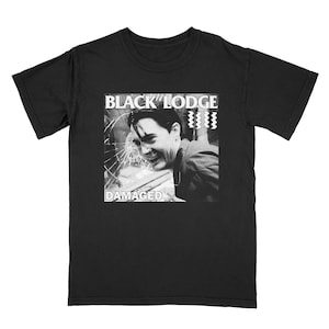 Puede incluir: Camiseta gráfica en blanco y negro con la imagen de un hombre con una ventana rota detrás. El texto "Black Lodge Damaged" está impreso en la camiseta.