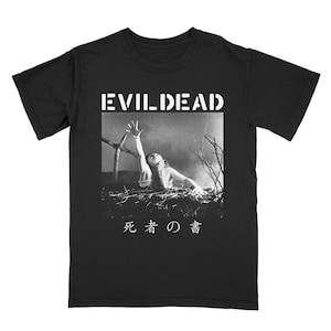 Puede incluir: Camiseta negra con un gr&aacute;fico blanco de una persona que se estira desde una pila de ramas. El texto "EVIL DEAD" est&aacute; por encima del gr&aacute;fico y "死者 の 聲" est&aacute; por debajo del gr&aacute;fico.