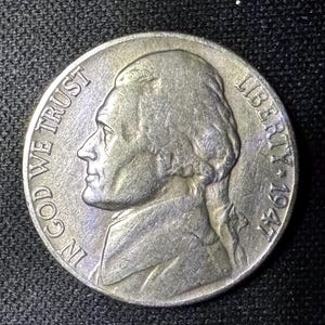 Peut inclure: Une pièce de cinq cents Jefferson de 1947. L'avers présente un profil de Thomas Jefferson, avec les inscriptions "IN GOD WE TRUST" et "LIBERTY". La pièce mesure environ 2,1 cm de diamètre.