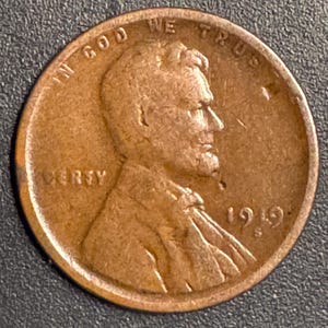 Può includere: Una moneta Lincoln del 1949, color rame. Il dritto presenta un profilo di Abraham Lincoln, con le scritte "IN GOD WE TRUST" e "LIBERTY". È visibile anche l'anno "1949".