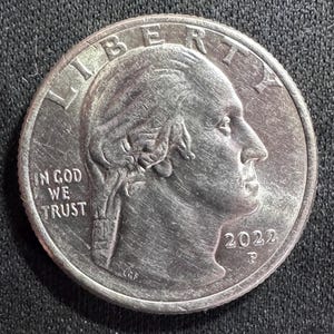 May include: A silver quarter coin with the profile of George Washington facing left. The coin features the inscriptions "LIBERTY" and "IN GOD WE TRUST", along with the year "2022".
