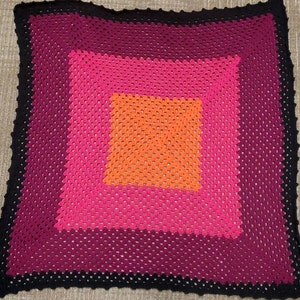 May include: A crocheted throw blanket with a multi-colored square pattern. The blanket is made with black, pink, red, and orange yarn.