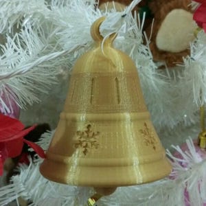 May include: A gold-colored bell ornament with a snowflake design. The bell is hanging from a white artificial Christmas tree.
