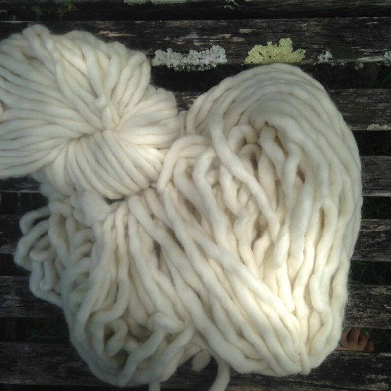 May include: A large pile of white yarn, likely wool, in a loose, fluffy arrangement. The yarn is thick and soft, with a natural, unbleached appearance.