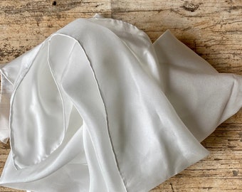 May include: A white silk scarf, folded and arranged on a wooden surface.