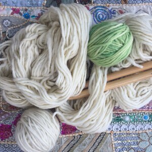 May include: White yarn with wooden knitting needles and a green ball of yarn.